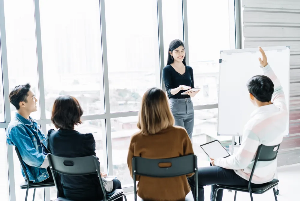 An instructor leading a small-group coaching session in a bright modern classroom, illustrating Coach2Reach's online education and training platform